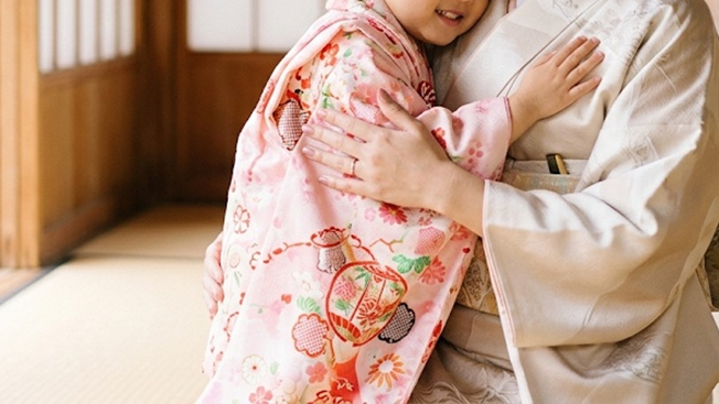 七五三の着物を着た子どもを優しく抱きしめる母親の姿。首から下の画角で、上品な和装と手元、温かみのある和室の雰囲気が伝わる写真。